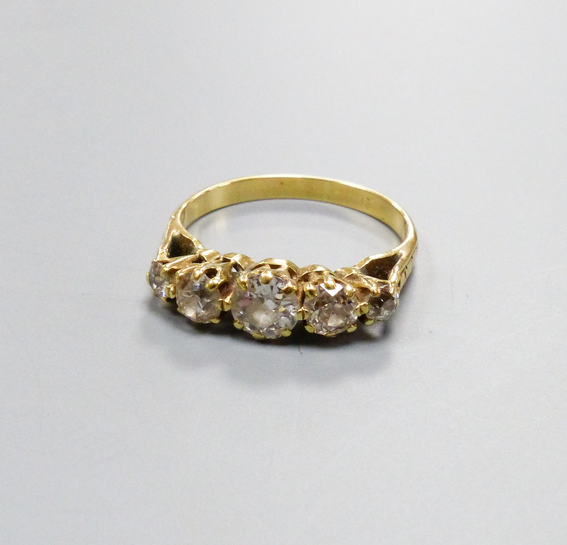 A five-stone diamond ring, yellow metal setting, claw-set with carved shoulders, size N, gross 3 grams.